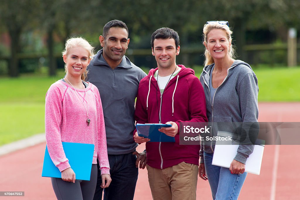 Four Happy Gym Coaches Two male and two female gym teachers standing on running track smiling at camera. Physical Education Stock Photo