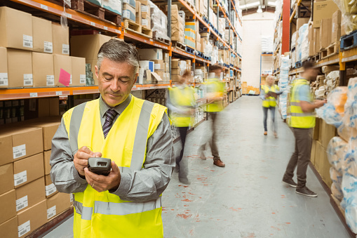Smiling male manager using handheld in a large warehouse