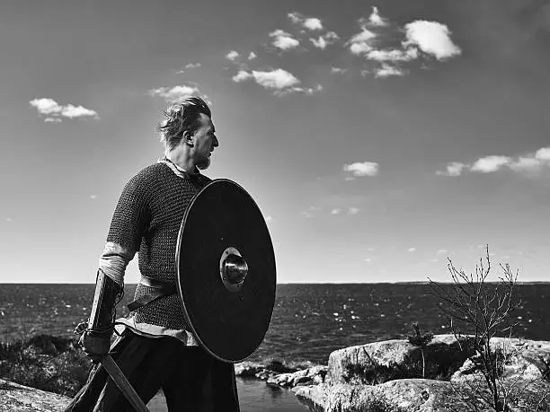Medieval viking warrior wearing chainmail, he has the sword and the shield, north nature on background, black and white image