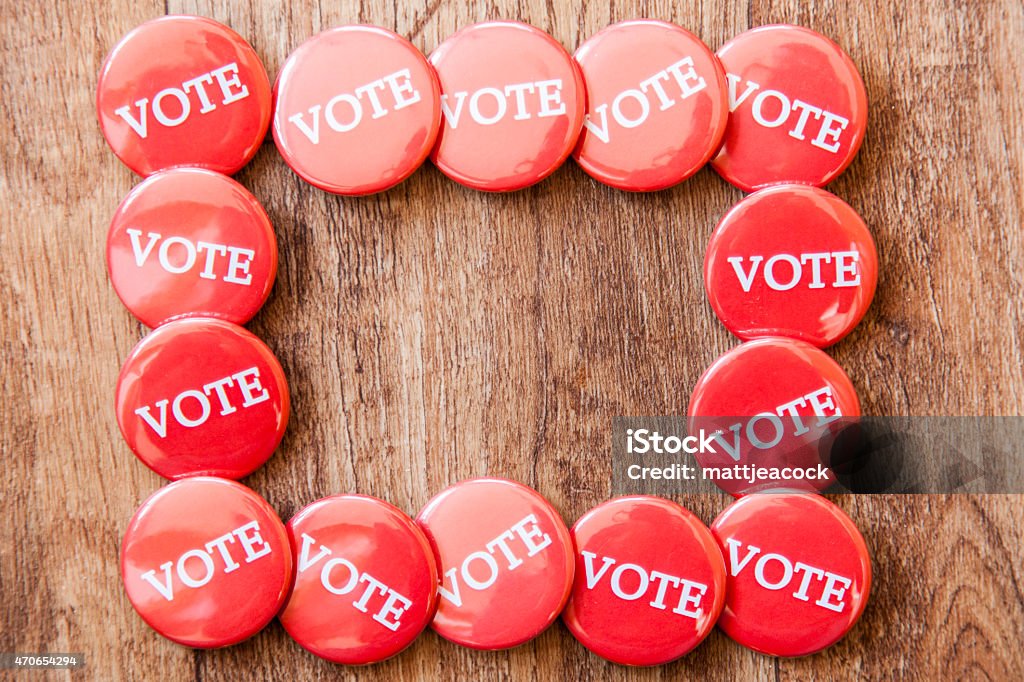 Collection of red voting badges on a wooden background Collection of red voting badges on a wooden background. The badges are circular with the word vote written in white capital letters. 2015 Stock Photo