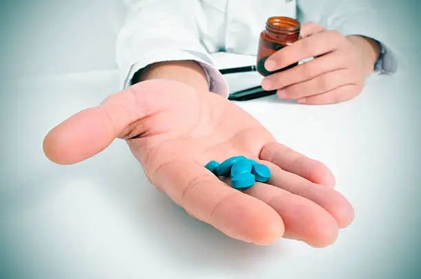 a doctor in a consulting room with a pile of blue pills in his hand