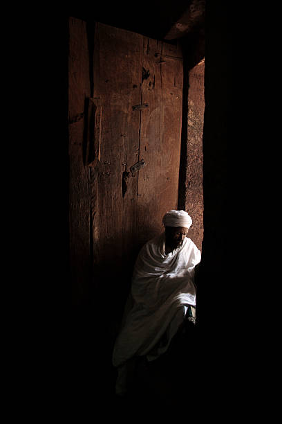 Ethiopian Priest Lalibela, Ethiopia - August 23, 2007: An Ethiopian priest read a bible in the light.Rock hewn churces make up the UNESCO world heritage site of Lalibela. each church is home to an orthodox priest. the priests spent their days studying the bible and acting as guides for toursits. the church of saint george lalibela ethiopia stock pictures, royalty-free photos & images