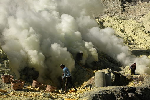Kawah Ijen, Indonesia - August 9, 2011: Miners collect sulphur in the fumes of toxic volcanic gas at s the ulphur mines in the crater of the active volcano of Kawah Ijen, East Java, Indonesia.
