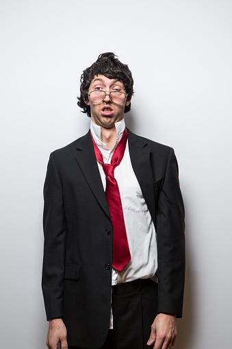 A funny man in business attire looks at the camera with an exhausted, confused, and disoriented expression on his face, his clothes messy and rumpled and his tie hanging partially off.  Representing boredom, lack of sleep, or dissatisfaction with work or job.  Vertical portrait.