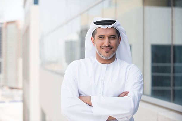 Arab businessman portrait outside office building A photo of confident and smiling mid adult arab businessman. Emirati man is wearing tradition clothing. Portrait of middle eastern professional standing arms with crossed outside office building. Dubai, United Arab Emirates, Middle East west asian ethnicity stock pictures, royalty-free photos & images