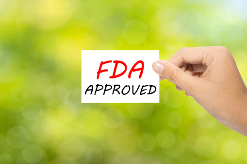 Hand holding a paper FDA APPROVED on green background
