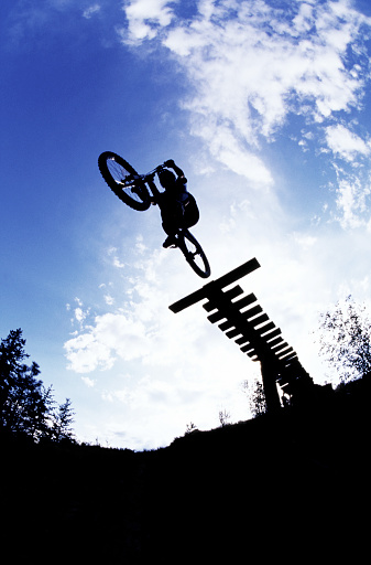 A male mountain bike rider rides off a wooden ramp on a downhill bike trail.