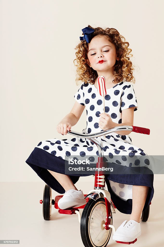 Girl in spots on tricycle Girl in spotty dress on tricycle holding candy 2015 Stock Photo