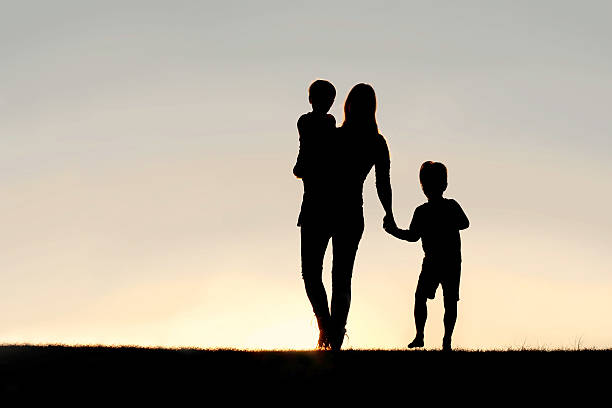 silhouette of a madre y young children holding hands at - familia con dos hijos fotografías e imágenes de stock