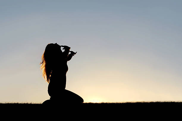 silhueta de mulher ajoelhada em oração e entregue-se - mulher de joelhos orando - fotografias e filmes do acervo