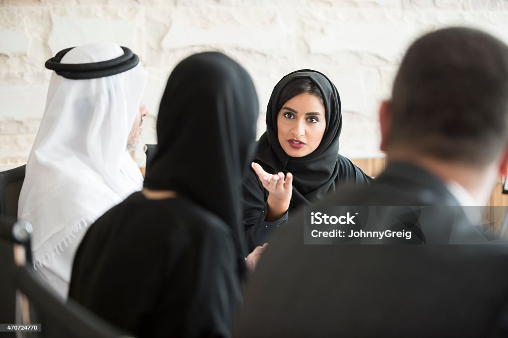 Confident Arab businesswoman in business meeting A photo of young and confident Arab businesswoman discussing in a meeting. Emirati woman wearing traditional abaya. Middle Eastern professional female is gesturing towards colleague while sitting in board room meeting. United Arab Emirates Stock Photo