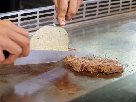 Close Up View of a Japanese Chef Deliberately Preparing and Cooking Traditional Beef teppanyaki on a hot plate