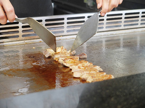 Close Up View of a Japanese Chef Deliberately Preparing and Cooking Traditional Pork teppanyaki on a hot plate