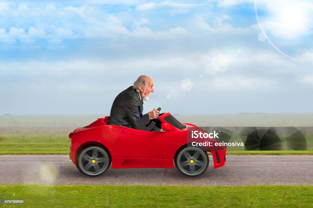 senior man driving a toy racing car senior man in a suit driving a toy racing car Humor Stock Photo