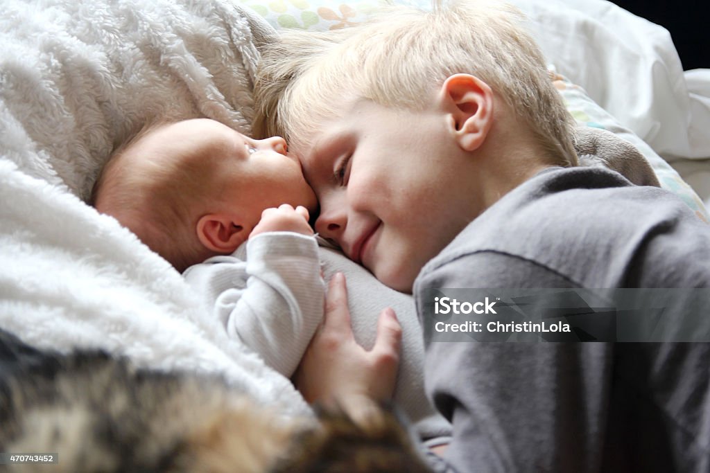 Big Brother Looking at Newborn Baby with Love A 5 year old big brother is hugging, smiling, and looking at his newborn baby sister as they sunggle in bed. Baby - Human Age Stock Photo