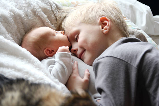 Big Brother Looking at Newborn Baby with Love A 5 year old big brother is hugging, smiling, and looking at his newborn baby sister as they sunggle in bed. sibling stock pictures, royalty-free photos & images