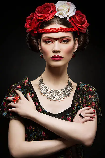 Beautiful young woman with bright red make up looking like Frida Kahlo. Over black background
