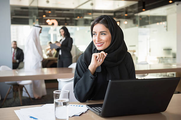 jovem emirati mulher de negócios, olhando para longe na mesa de reunião - istockalypse imagens e fotografias de stock