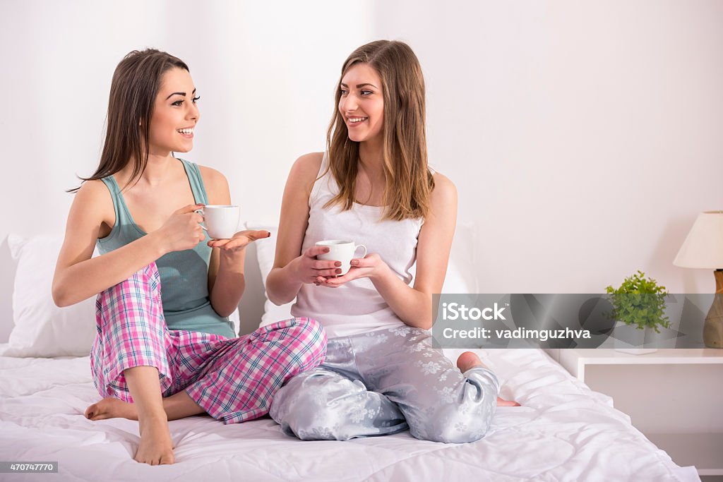 Girlfriends at home Pajama party. Young beauty girls in pajamas drinking a cup of tea in bed at home. Pajamas party Slumber Party Stock Photo