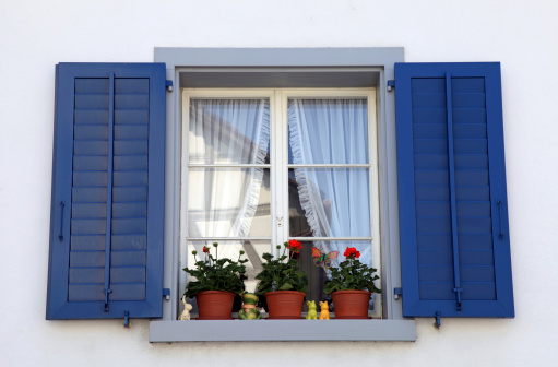 rustic window with blue shutters and flower pots in white rural house, Switzerland.
