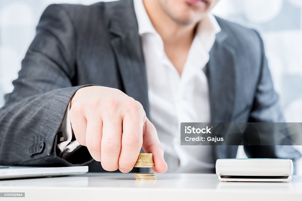 Successful businessman counting money Successful businessman sitting at his desk counting gold coins in a conceptual image, closeup view of his torso with focus to his hand. 2015 Stock Photo