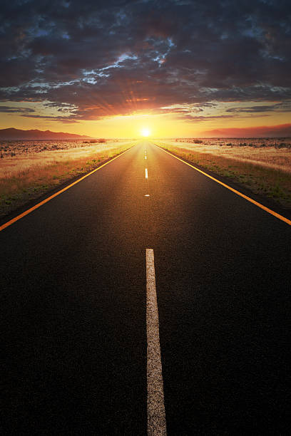 Straight asphalt road leading into sunlight stock photo