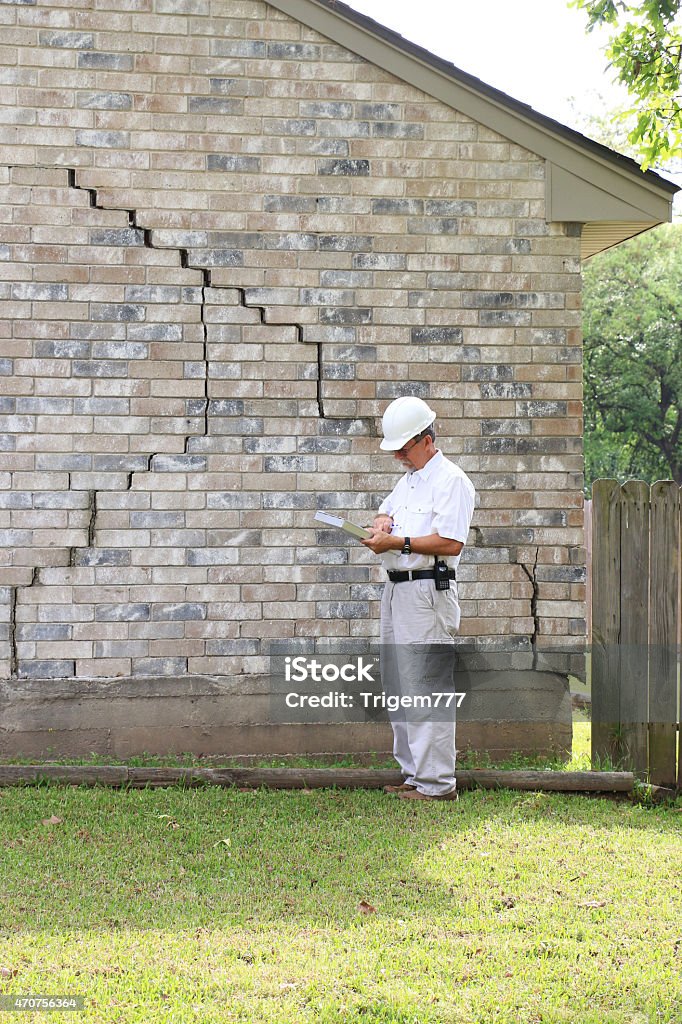 Construction worker analysing house foundation damage Inspector inspecting home’s foundation is experiencing settlement (collapse). Eventually the brick veneer begins to separate from door and window frames. Finally framing and roof problems occur, as well as plumbing problems. Foundation problems don’t get better without professional repair and house leveling. It is better to take action sooner rather than later. Cracked Stock Photo