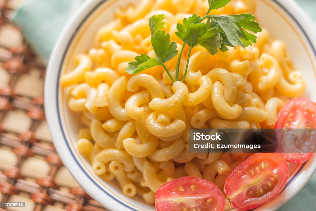 Elbow Macaroni and Cheese Delicious macaroni and cheddar cheese with fresh sliced grape tomatoes and parsley sprig 2015 Stock Photo