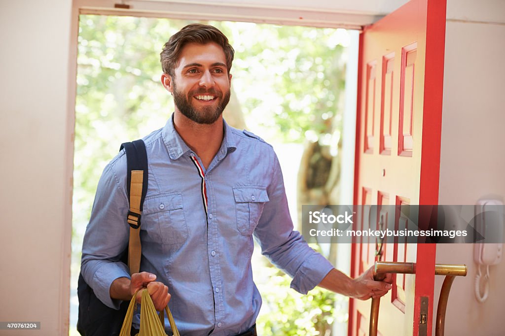 Young Man Returning Home For Work With Shopping Young Man Returning Home For Work With Shopping, Smiling Arrival Stock Photo