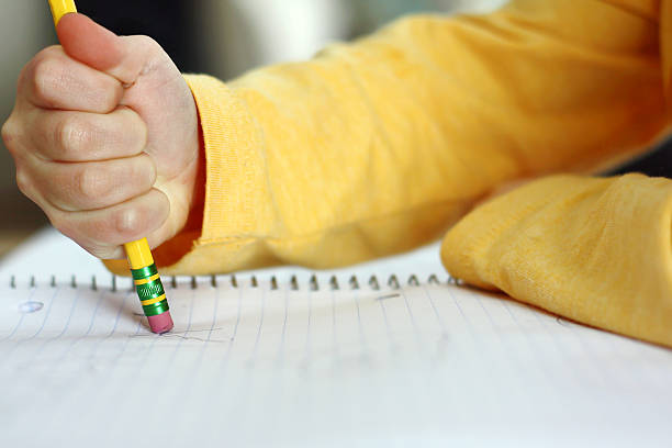 a child has made a mistake while writing and is holding a pencil and erasing on white notebook paper