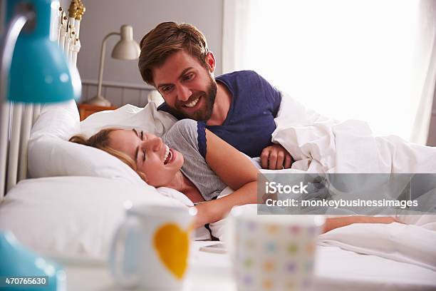 Young Couple Relaxing And Laughing In Bed Together Stock Photo - Download Image Now - 20-29 Years, 2015, Adult