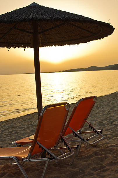 istock Two orange chairs and stray parasol on beach at sunset 470768542