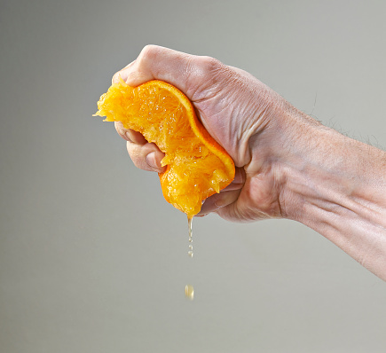 Fresh Squeezed Orange Juice by male hand and juice falling with droplets