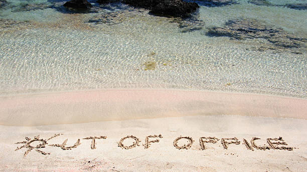 Out of office written on sand on clear beach