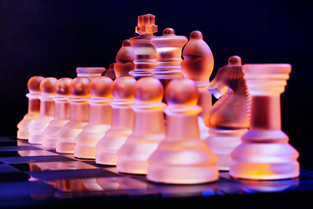 szkło szachy na chessboard oświetlony przez światło niebieskie i pomarańczowe - armed forces black yellow chess pawn zdjęcia i obrazy z banku zdjęć