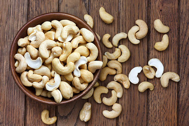 Bowl of halved cashew nuts in a wooden bowl Wooden bowl of cashew nuts from above. On dark wood. cashew photos stock pictures, royalty-free photos & images