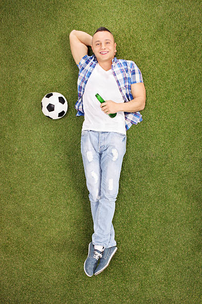 istock Young football fan lying on grass and drinking beer 470797244