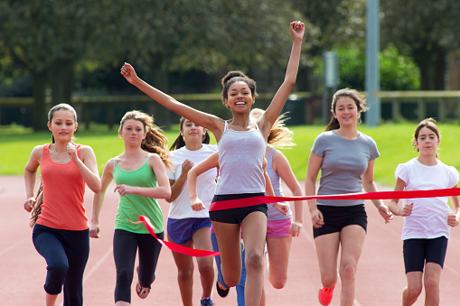 Group of teenage girls crossing the finish line of a track race.