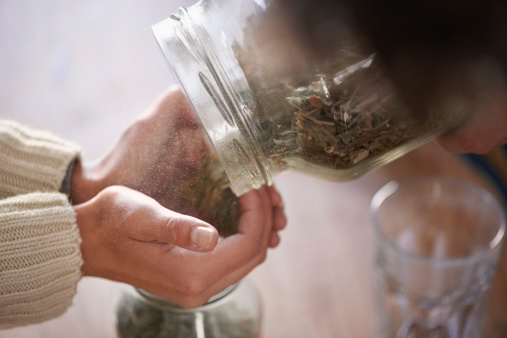 Cropped shot of a young woman's hands putting tea leaves in a jar