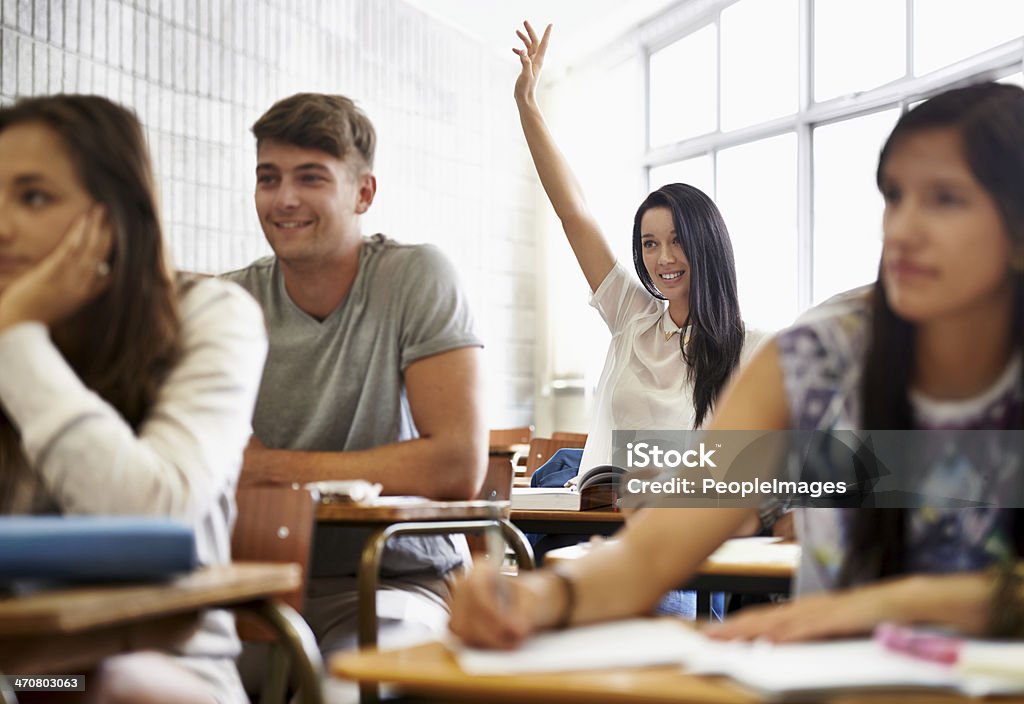 Working her way towards a distinction A young woman raising her hand as she sits in a varsity class surrounded by her peers 20-24 Years Stock Photo