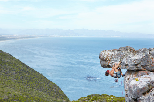 An experienced female climber scaling a rock face with a beautiful vista behind her