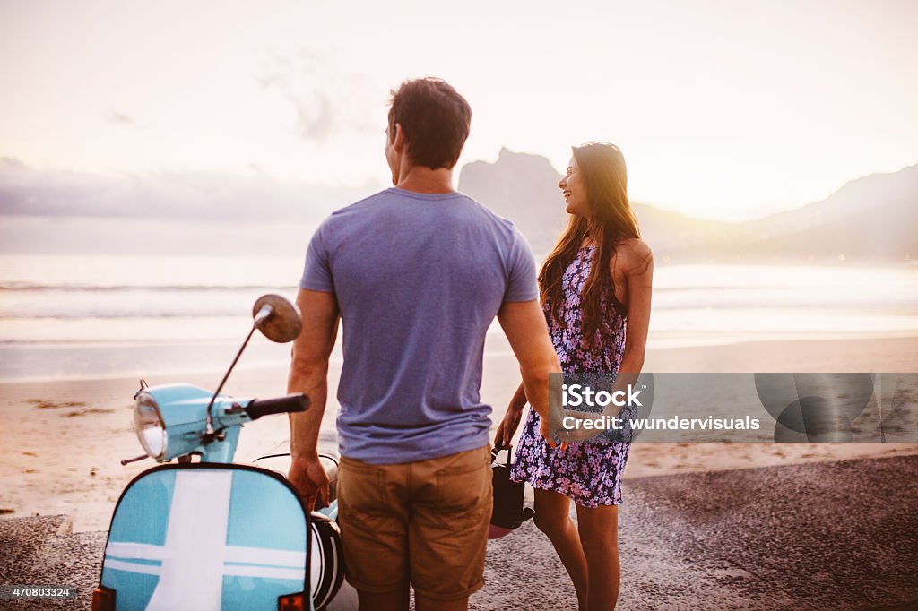 Loving couple at the beach with their scooter Loving couple looking out at the sea at the beach standing next to their scooter Motor Scooter Stock Photo