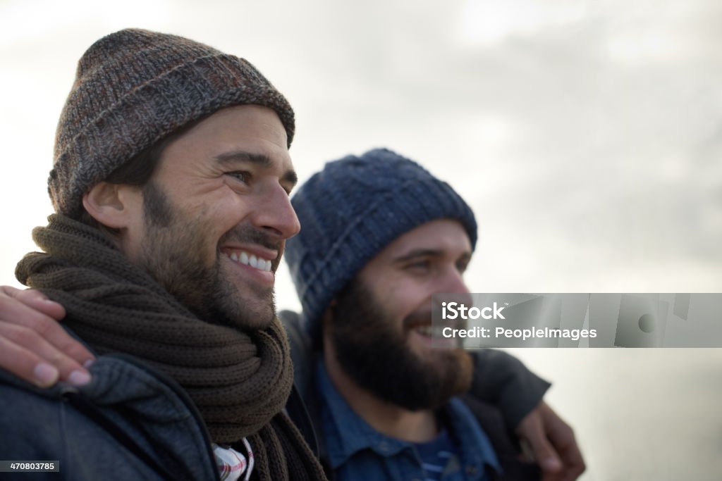 Wrapped up against the crisp ocean chill Two handsome young fishermen standing on the beach on a cool morning Men Stock Photo