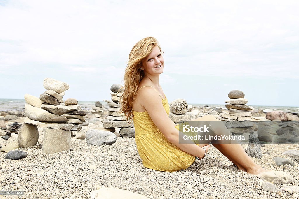 Beautiful Teen Girl at the Beach A beautiful teen girl smiles at the camera ash she sits on the beach, surrounded by inuksuit. Copy space in sky. Adolescence Stock Photo