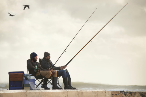 Shot of two young men fishing off a pier