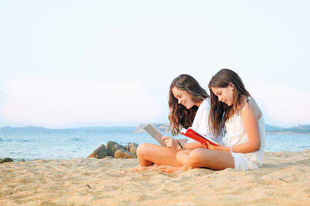 две девочки, чтение на пляже - child beach digital tablet outdoors стоковые фото и изображения