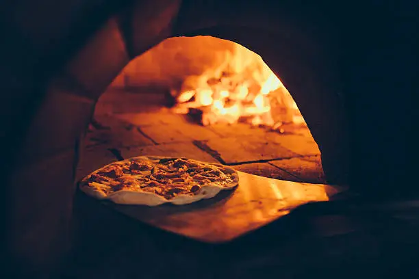 Vintage style image showing a traditional wood fire pizza oven with a fresh pizza being put inside it