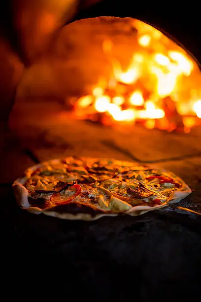 Fresh vegetarian pizza being carefully placed inside a traditional wood fire oven