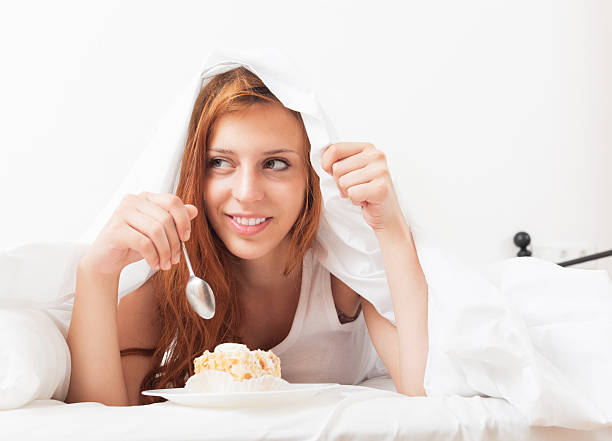 istock Young woman eating sweet cake under sheet in bed 470820977