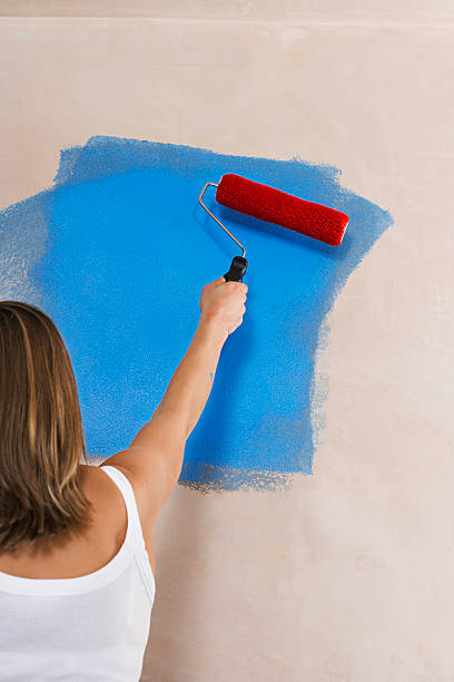 istock Woman Painting Wall Blue With Paint Roller 470826213